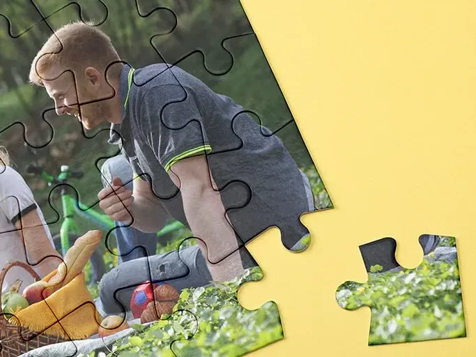 Kartonnen fotopuzzel met een picknickfoto en een los stukje op een gele ondergrond